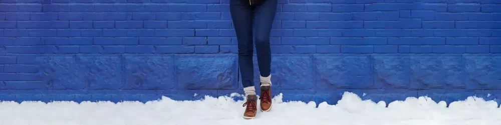 Close up of person leaning against a blue brick wall in the snow wearing Kamik Rouge Hike 3 boots